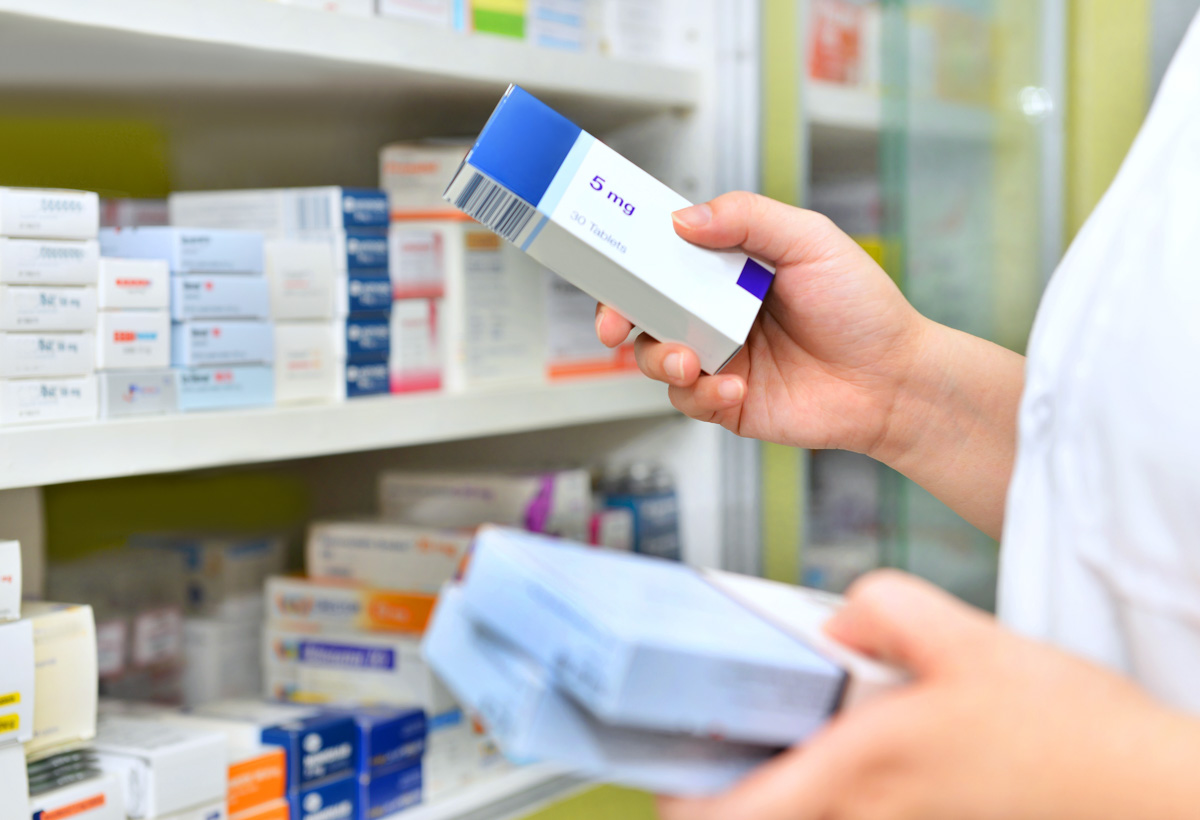 Mitarbeiter einer Apotheke sortiert verschiedene Medikamente vor einem Regal