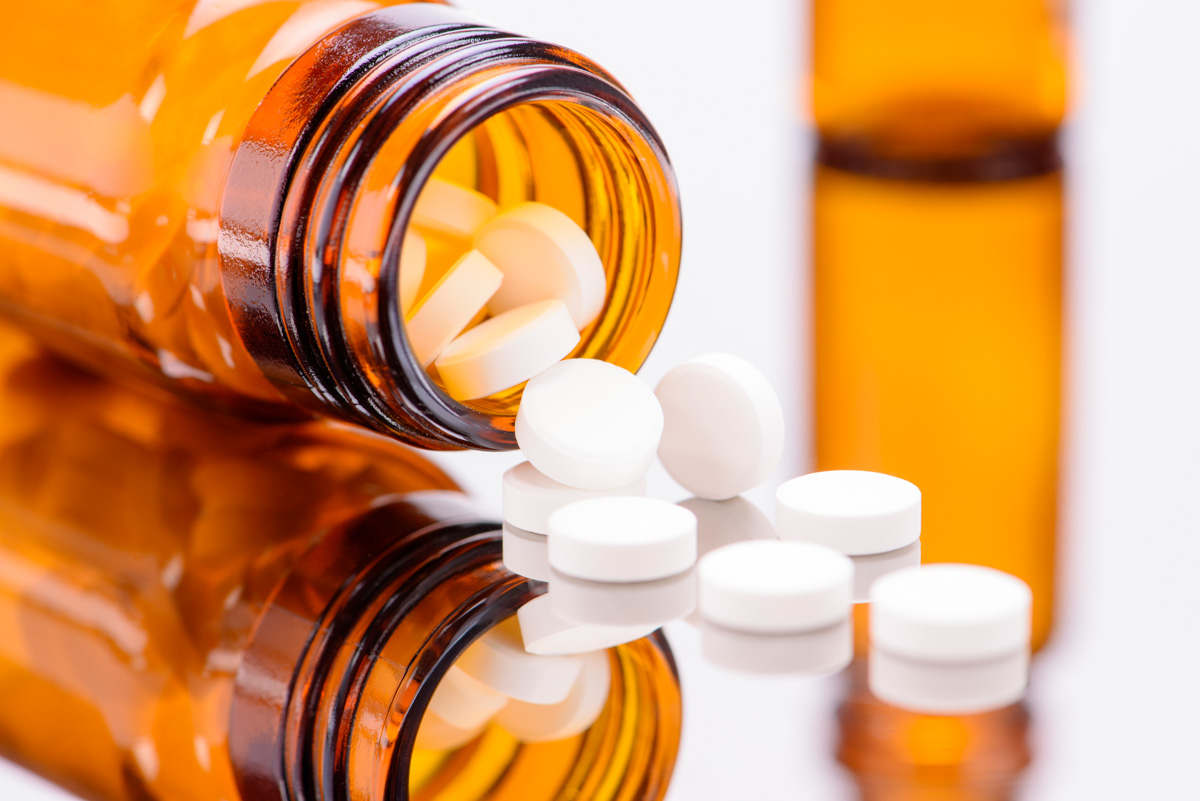 Nahaufnahme eines umgekippten braunen Behälters mit weißen Schüssler Salze-Tabletten auf einem reflektierenden Tisch